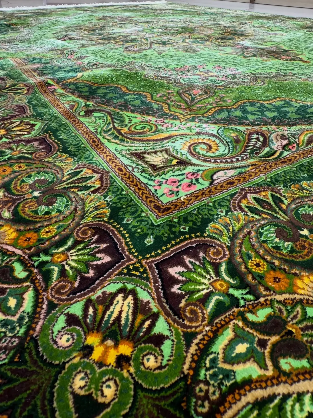 Low-angle close-up of the green patterned border and pile of Qom silk rug PRR-HM-003