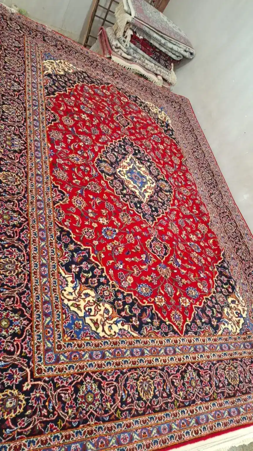 Vue oblique du tapis de Kachan PRR-KH-029 au médaillon royal Herati, champ rouge et médaillon bleu nuit
